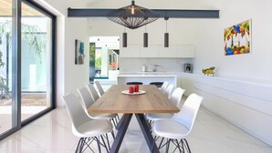 A modern dining area with a wooden table, white chairs, and pendant lighting. - Casa Bela with heated pool and luxury of 5 stars (Klimno (Krk))