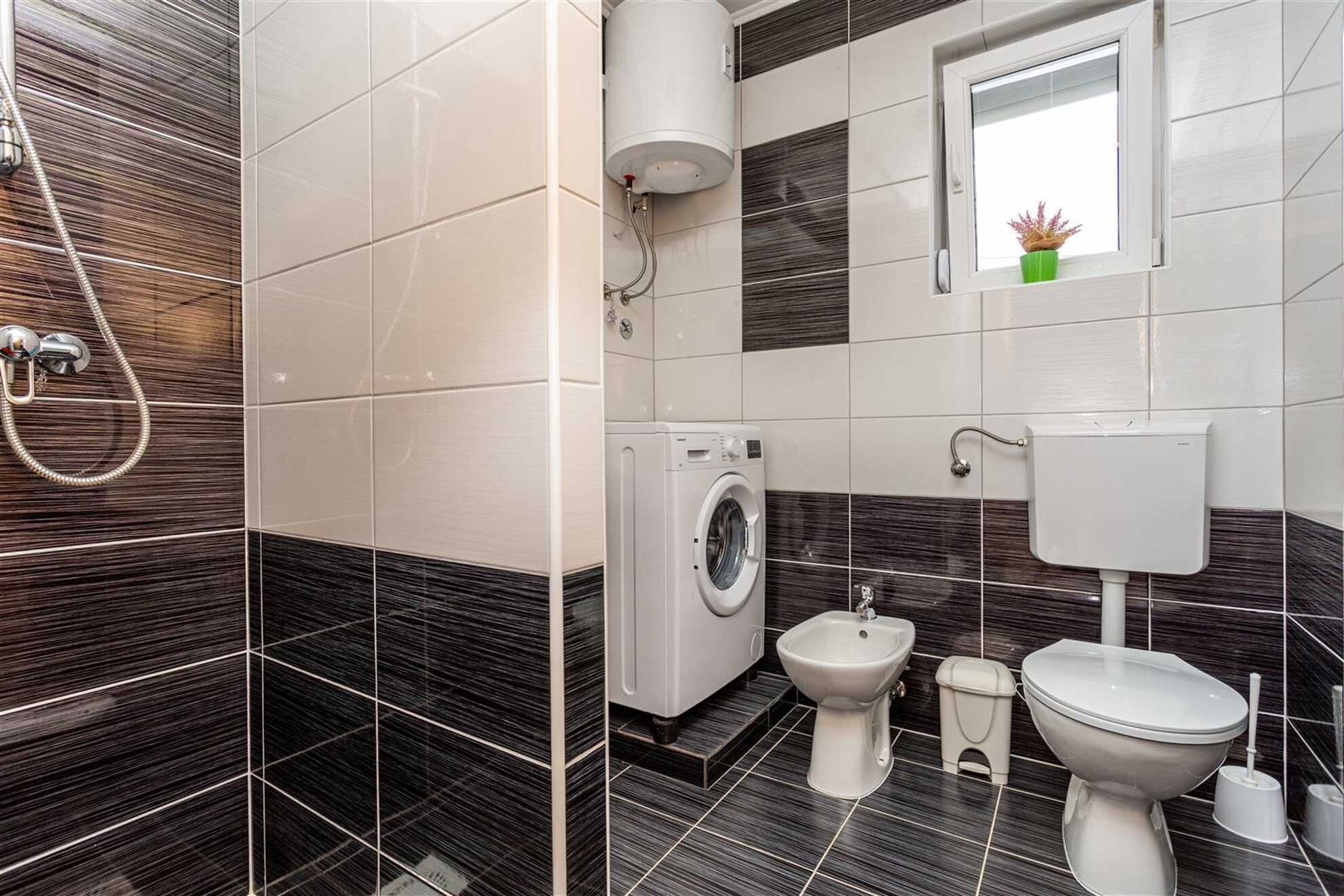 Un baño moderno con lavadora, bidé, inodoro y una ventana con una planta.
