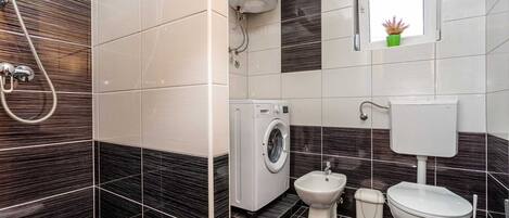 Un baño moderno con lavadora, bidé, inodoro y una ventana con una planta.