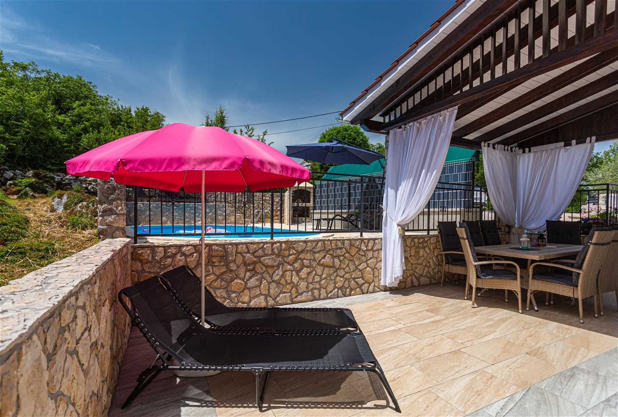 A poolside area with a stone wall, a black lounge chair, and a table with chairs.