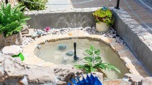 Un petit élément décoratif aquatique avec une fontaine, entouré de rochers et de plantes.