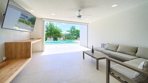 Una sala moderna con una televisión de pantalla plana montada en la pared, un banco de madera, un sofá, una mesa de centro y un ventilador de techo.