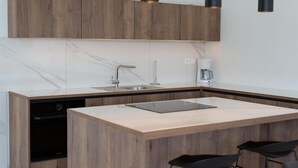 Una cocina moderna con armarios de madera, encimera de mármol, lavavajillas integrado, cafetera y una tablet en la isla.