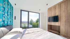 Un dormitorio con una cama grande, un televisor montado en un mueble de madera y vistas a zonas verdes a través de una puerta corrediza.
