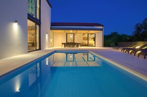 A modern house with a swimming pool, a patio with outdoor furniture, and a well-lit interior.