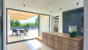 Un interior moderno con techo de madera, un vidrio que da a un patio exterior y un mueble de madera con jarrones decorativos.