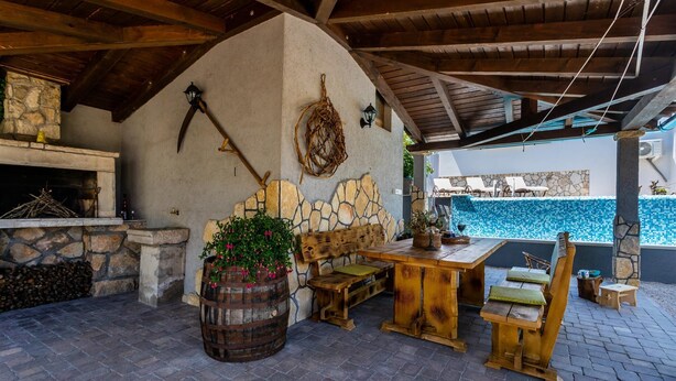Un patio esterno rustico con pareti in pietra, un tavolo di legno, panche e un camino in pietra.