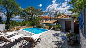 Area piscina con lettini, un piccolo edificio con tetto in tegole e vista sul paesaggio.