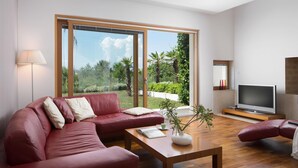 A modern living room with a red leather sofa, a wooden coffee table, and a TV on a wooden stand. Large windows offer a view of a garden. - Exclusive and modern Casa Vidmar with a large swimming pool (Klimno (Krk))