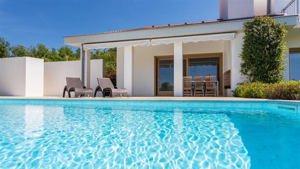 A swimming pool with clear water, surrounded by lounge chairs and a covered patio area. - Exclusive and modern Casa Vidmar with a large swimming pool (Klimno (Krk))