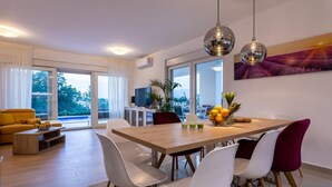 A modern dining area with a wooden table, white chairs, and a large window offering a view of greenery. - Villa Zarra with heated pool, jacuzzi, sauna and Seaview (Klimno (Krk))