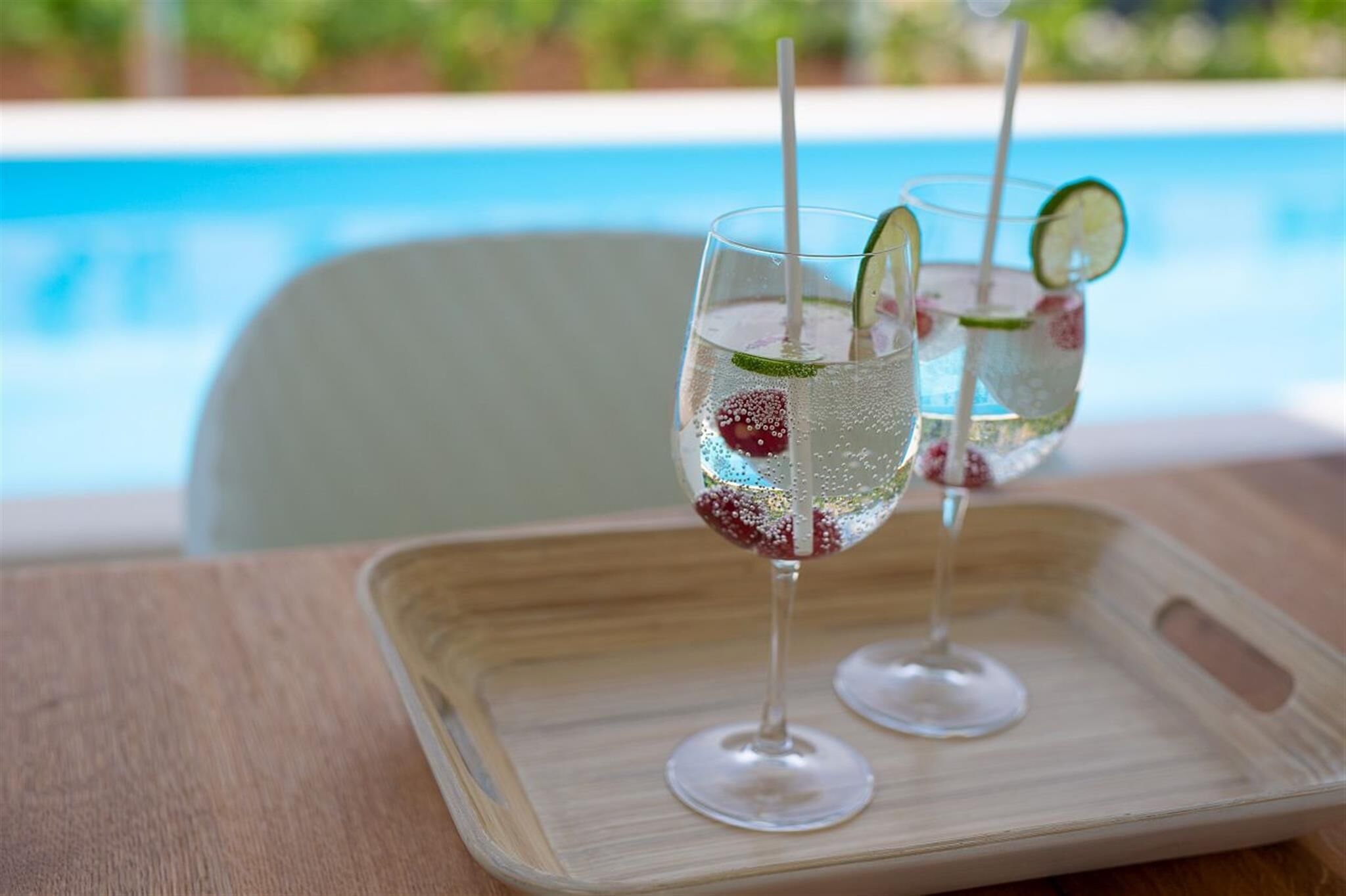 Two glasses of a beverage with lime and strawberry garnish on a tray by a pool.