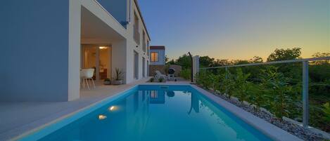 A modern house with a swimming pool, a covered patio, and a view of the surrounding landscape.