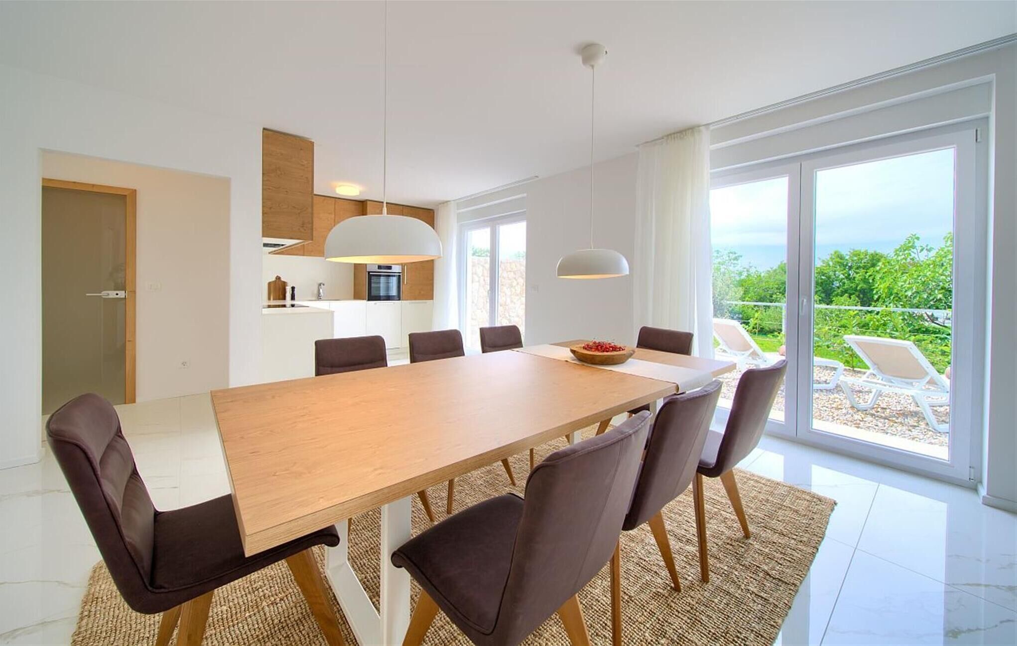 Ein moderner Essbereich mit einem langen Holztisch, dunklen Stühlen und Blick ins Freie durch große Fenster.