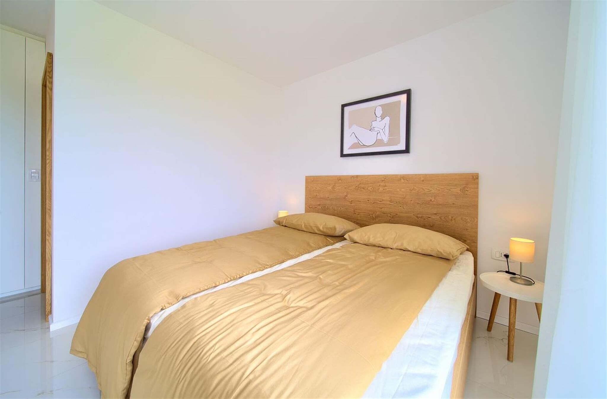 A bedroom with a bed, a bedside table with a lamp, and a framed picture on the wall.