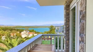 A balcony with a wooden table and chairs, overlooking a coastal landscape with mountains and a body of water. - Residencia La Famiglia with heated swimming pool and beautiful Seaview (Klimno (Krk))