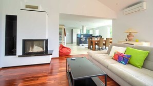 A modern living room with a fireplace, a sofa with colorful cushions, a dining area, and a kitchen in the background. - Residencia La Famiglia with heated swimming pool and beautiful Seaview (Klimno (Krk))