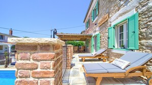 Ein Steingebäude mit Pool, Holzliegen und einer Pergola.