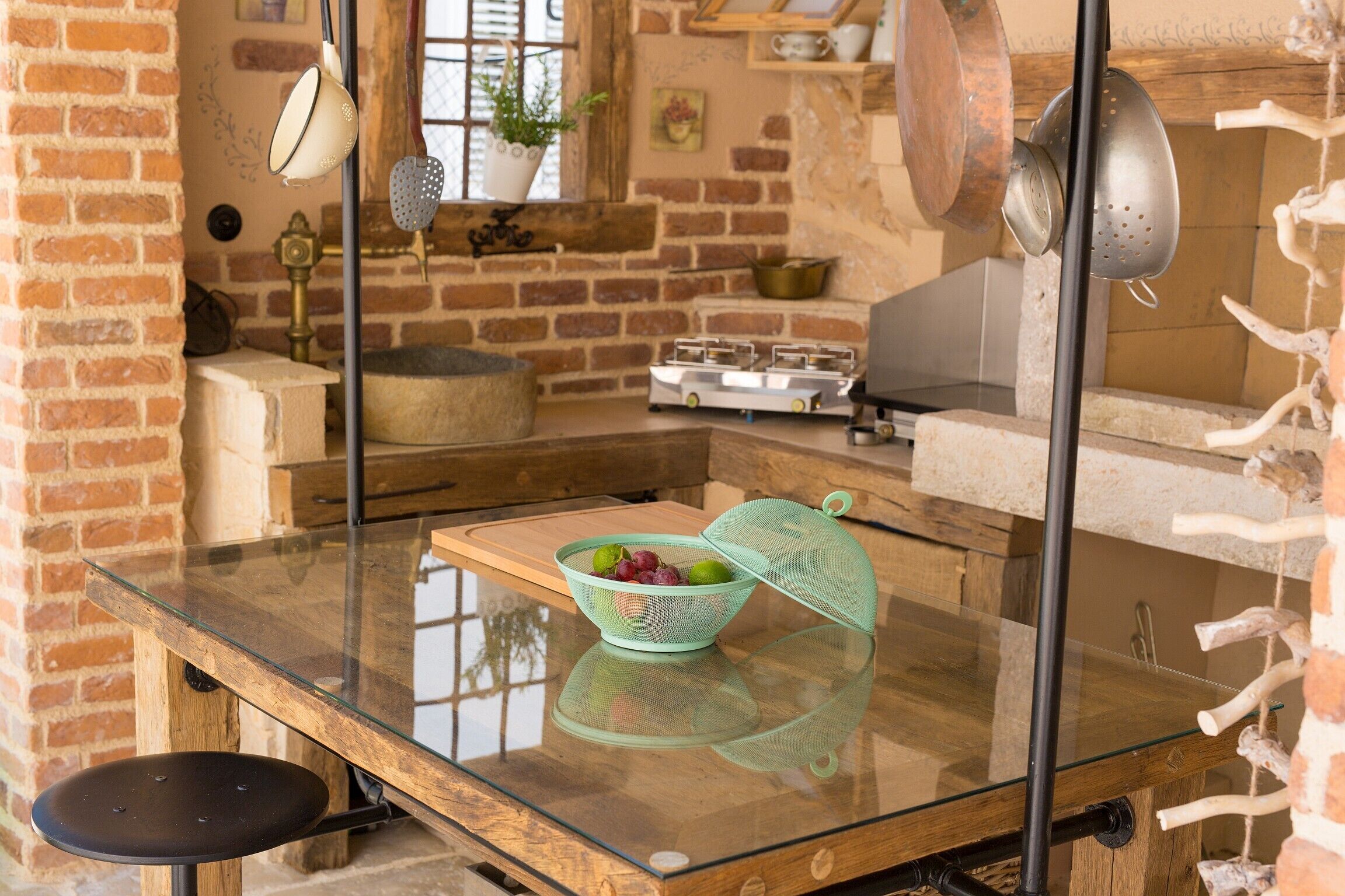 Una cocina con una mesa de vidrio, un colador lleno de frutas y una pared de ladrillo.