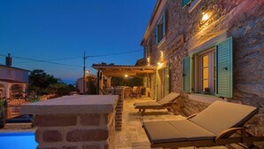 Ein Steinhaus mit Pool, Sitzgelegenheiten im Freien und einer überdachten Terrasse.