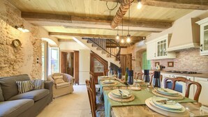 Ein rustikaler Essbereich mit Holztisch, gedeckt für eine Mahlzeit, einer Couch und einer Treppe, die zu einer oberen Ebene führt.
