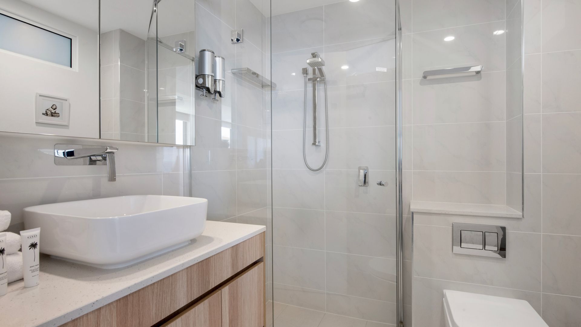 A modern bathroom with a large white sink, a glass shower enclosure, and a toilet.