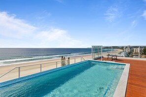 A clear view of a swimming pool with a wooden deck, overlooking a beach and ocean. - Ocean Views Apartment with Rooftop Pool (Palm Beach)