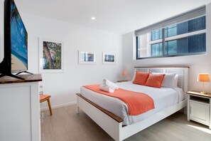 Un dormitorio moderno con cama, mesitas de noche, escritorio y ventana.