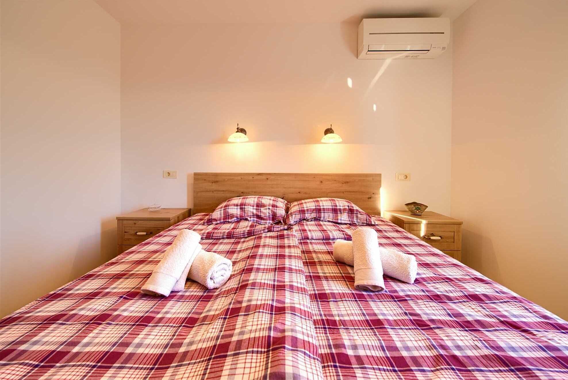 Une chambre à coucher avec une couvre-lit à carreaux, deux lampes de chevet, un climatiseur et une tête de lit en bois.