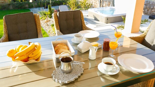 Een ontbijt op een buitentafel met rieten stoelen, een jacuzzi en uitzicht op de tuin.