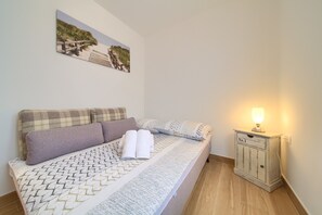 Een netjes opgemaakt bed met een bedsprei met dessin, een hoofdbord met ruitmotief en een nachtkastje met een lamp.