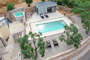 Zona de piscina al terrat amb una piscina rectangular, seients de relax i un edifici petit amb terrat pla.