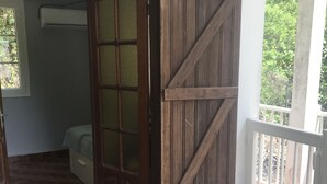 Ein Zimmer mit Fliesenboden, einem Bett, einer Holztür und einem Balkon mit Geländer.
