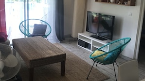 Ein Wohnzimmer mit einer Couch, einem Fernseher, einem Bücherregal und einem Fenster mit Vorhängen.