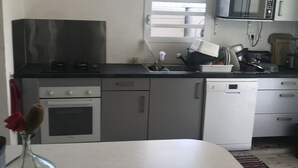 Eine Küche mit Herd, Backofen, Mikrowelle und Geschirrspüler. Ein Fenster mit Jalousien, ein Spülbecken und eine Arbeitsplatte mit verschiedenen Gegenständen sind ebenfalls vorhanden.