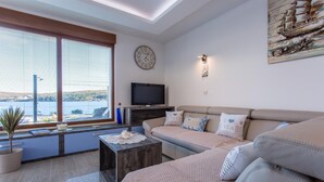 A living room with a sofa, a coffee table, a TV, and a large window overlooking a body of water. - Villa Ema with Seaview, swimming pool, garage, BBQ & playroom (Čižići (Krk))