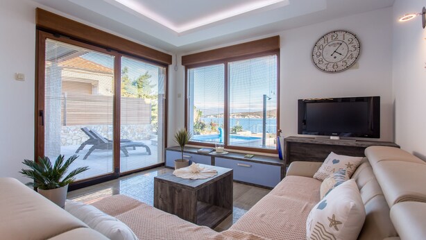 A modern living room with a large TV, comfortable seating, and a view of the sea through large windows. - Villa Ema with Seaview, swimming pool, garage, BBQ & playroom (Čižići (Krk))