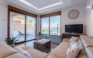Una sala de estar moderna con un televisor grande, asientos cómodos y vistas al mar a través de amplios ventanales.