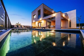 A modern building with a swimming pool, large windows, and outdoor seating areas. - Villa Maluja (Sukosan)