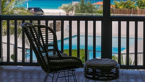 Un balcon avec un fauteuil et un pouf en osier, donnant sur une piscine et une plage.