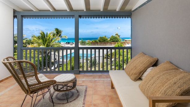Un balcon avec vue sur l’océan, une piscine et un espace détente avec un canapé et des fauteuils.