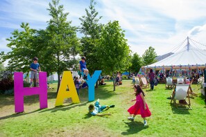 A grassy area with large colorful letters spelling 'HAY' and a white tent in the background.