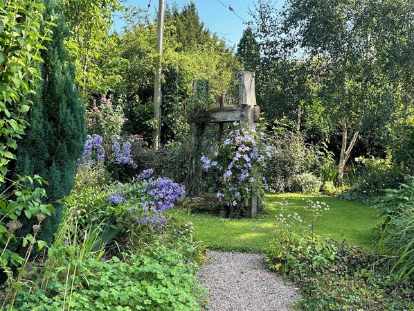 Um jardim com caminho de cascalho, diversas plantas e uma estrutura de madeira.