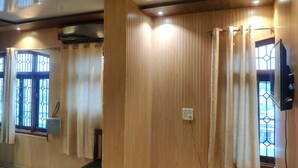 Una habitación con paneles de madera, un banco, un enchufe y una ventana con cortinas.