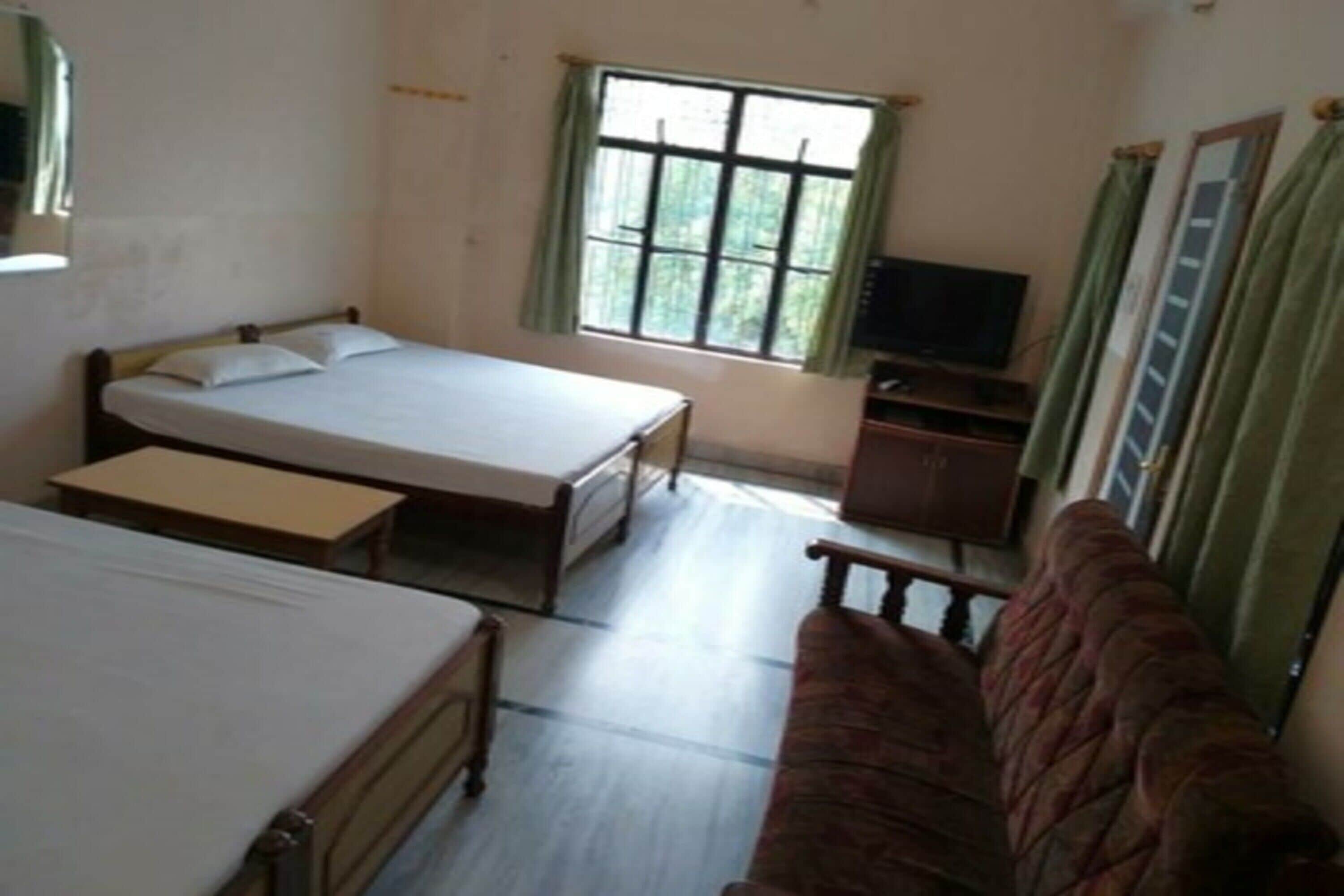 A room with two single beds, a sofa, a television, and a window with curtains.