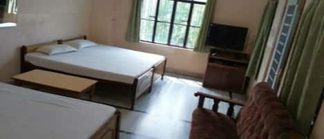 A room with two single beds, a sofa, a television, and a window with curtains.