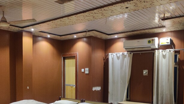 Habitación de hotel con dos camas de madera, un ventilador de techo, un equipo de aire acondicionado y un banco.