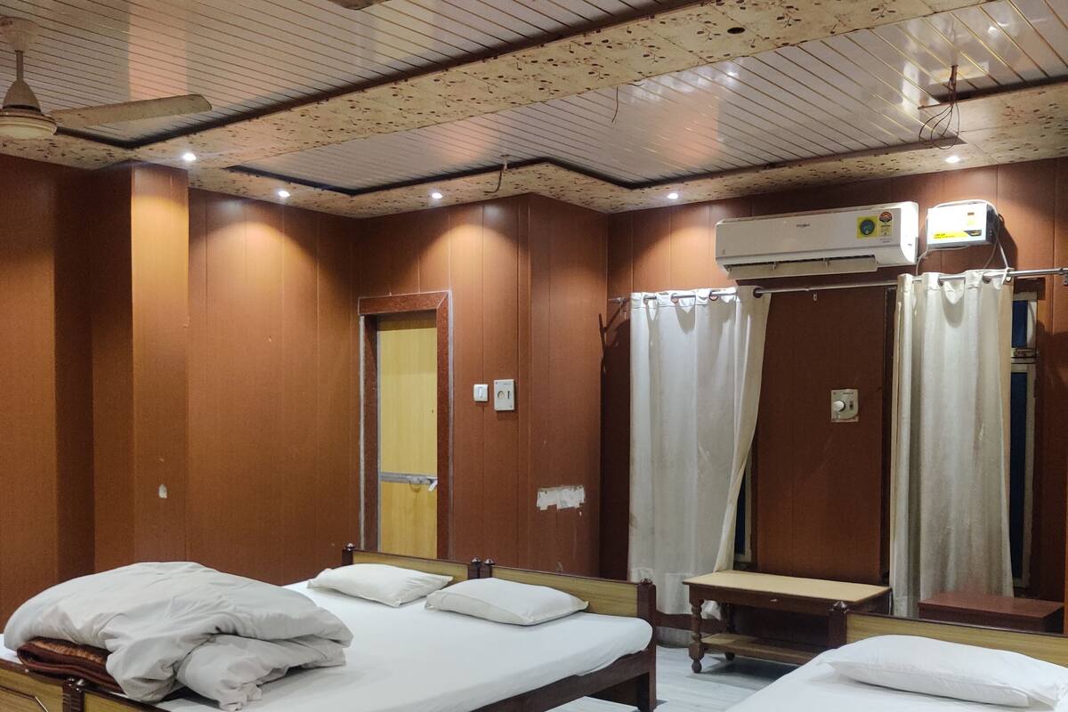 Hotellihuone, jossa on kaksi puista sänkyä, kattotuuletin, ilmastointilaite ja penkki.
