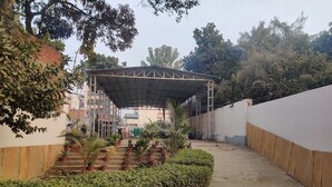 Un espacio al aire libre cubierto con escalones que llevan a un edificio, rodeado de follaje y un muro blanco.
