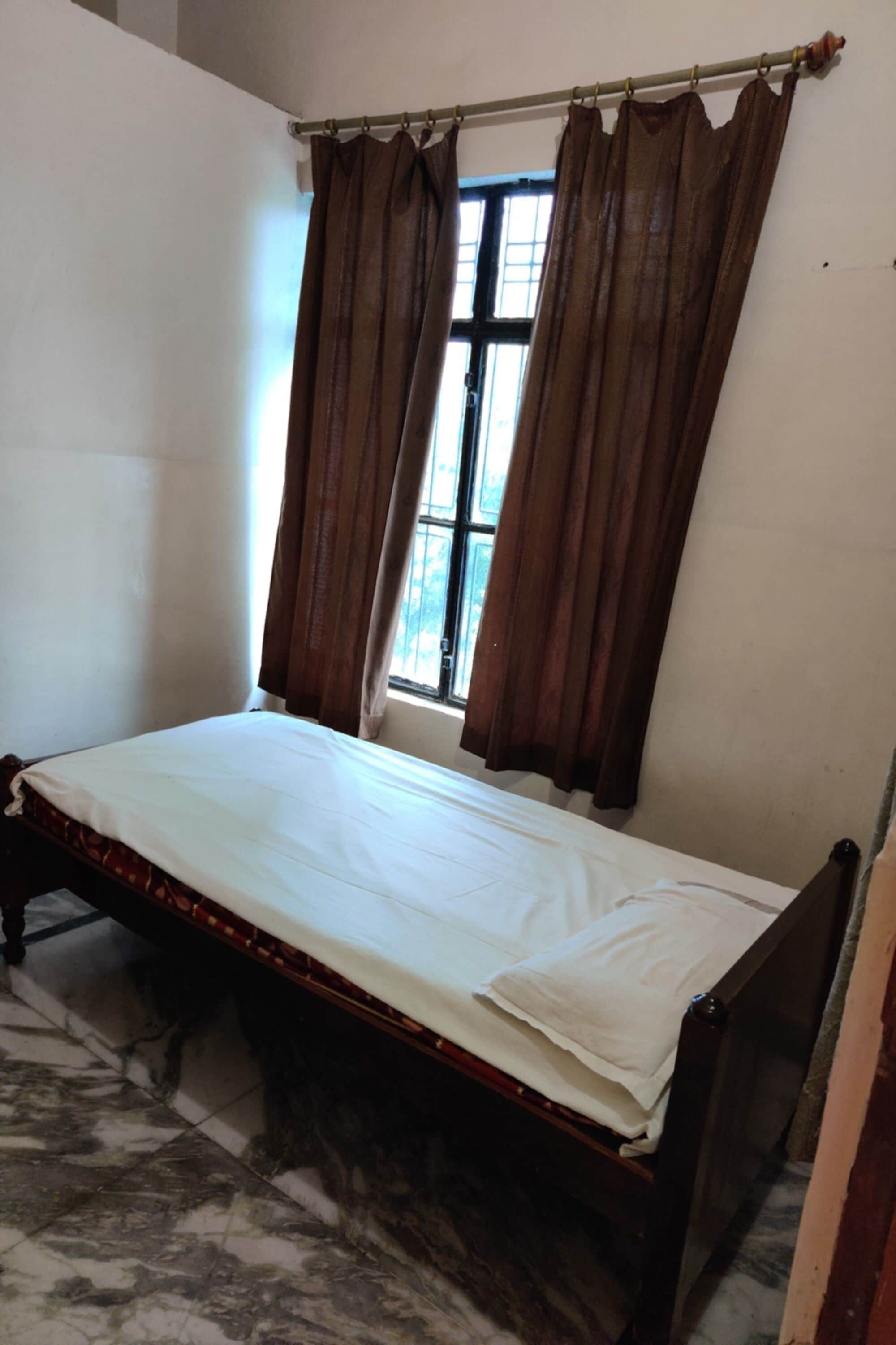A room with a single bed, a window with curtains, and a tiled floor.